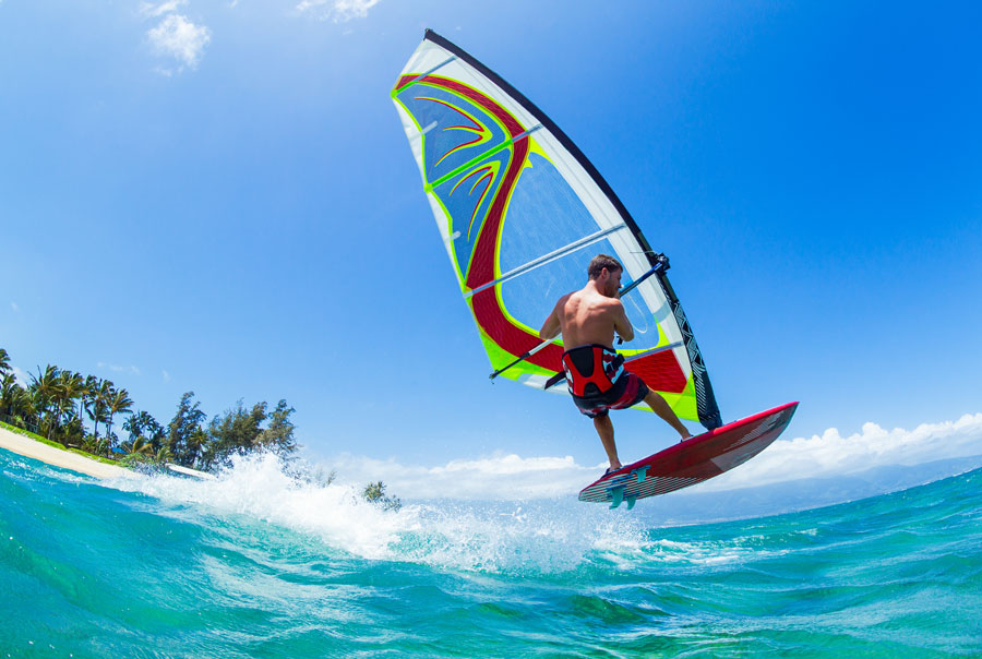 Thrills of Paradise 10 A windsurfer riding a wave in Sri Lanka. The windsurfer is in mid-air, with the sail above his head and the board beneath his feet. The water is clear and blue, and the sky is bright and sunny.