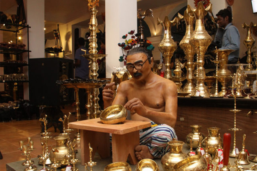 Thrills of Paradise 17 A craftsman meticulously crafting a brass bowl in a shop filled with traditional Sri Lankan brassware.